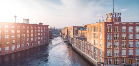  Tammerkoski flows between two old, red-brick factory buildings with glass windows in Tampella.