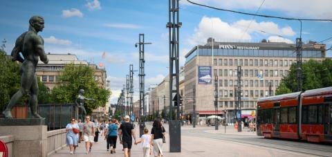 Ihmisiä kävelee Hämeensiltaa pitkin kesäpäivänä, vieressä ajaa ratikka.