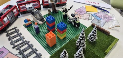 Legoratikka, legokaupunki, kortteja ja pieniä leikkipuita pöydällä.