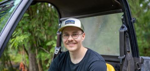 Henkilö istuu työkoneen kyydissä ja nojaa toisella kädellään rattiin.