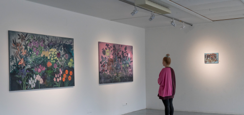 Henkilö katsoo värikkäitä ja suuria kukkatauluja taidegalleriassa.
