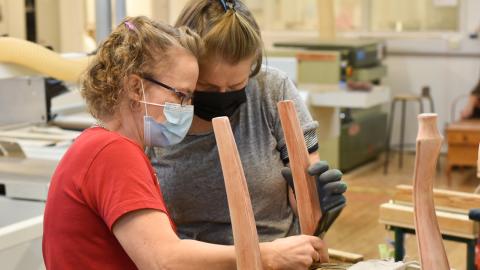 Kaksi henkilöä entisöi tuolia puukäsityöluokassa.