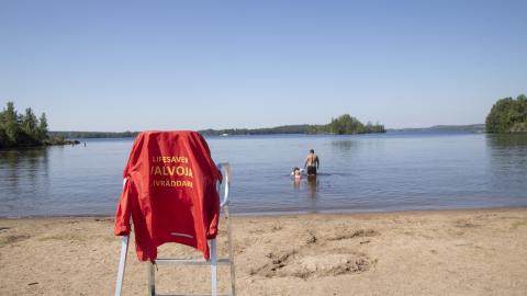Pyynikin uimarannalla uimavalvojan tuoli ja takki, vedessä ihmisiä uimassa.