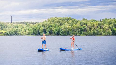 Kaksi henkilöä sup-lautailee järvellä.
