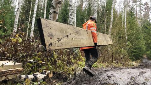 Henkilö kantaa pitkospuuta mutaisella polulla.