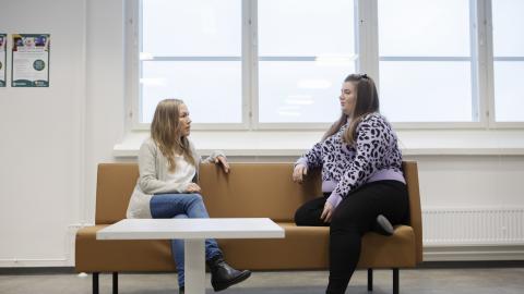 Kaksi henkilöä istuu sohvalla ja juttelee keskenään.