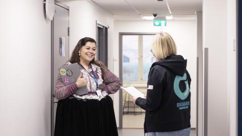 Kaksi henkilöä juttelee käytävällä. Toinen on romaniasussa ja toinen on pukeutunut Ohjaamon huppariin.