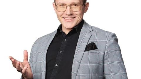 Tummahiuksinen mies seisoo kuvassa puvuntakki päällään ja hymyilee kameralle