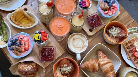 Pöydälle on katettu erilaisia ruokia kuten esimerkiksi puuroa, croisantteja, kahveja, vohveleita ja marjoja.