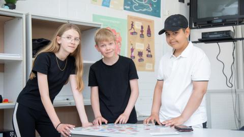 Kolme nuorta pelaavat pöydän ympärillä.