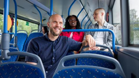 Mies istuu hymyillen bussin kyydissä.