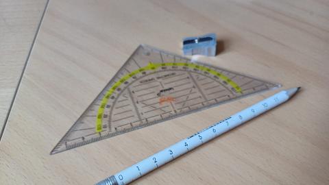 Kuvassa kynä, teroitin ja piirtokolmio.