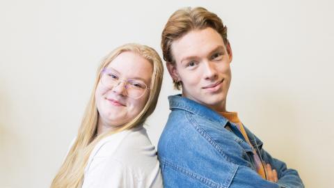 Venla ja Oliver istuvat selät vastakkain ja hymyilevät kameraan.