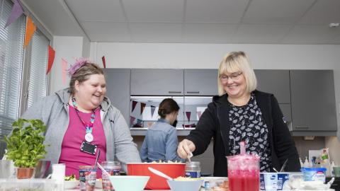 Kaksi henkilöä seisoo tarjoiluastioita täynnä olevan buffetpöydän takana.