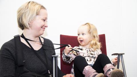 Äiti ja lapsi katsovat toisiaan hymyillen. Lapsi pitää kädessään äidin henkilökorttia.