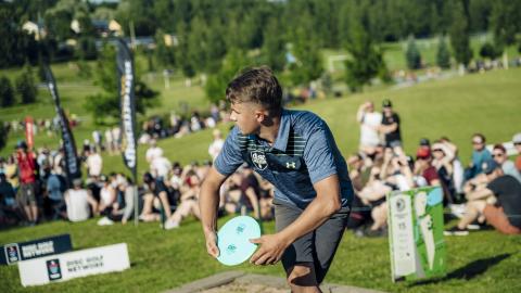 Henkilö frisbeegolfaa yleisön edessä.