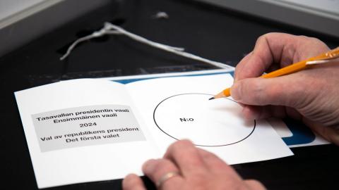 Äänestyslipuke äänestyskopin pöydällä ja kaksi kättä, joista toisessa on lyijykynä.