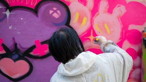 Nuori henkilö maalaa valkoisessa haalarissa graffitia.