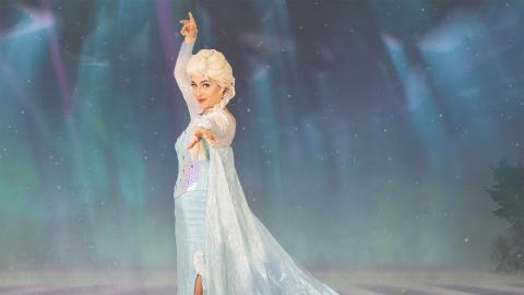 Lumikuningatar sinisessä pitkässä mekossa ja viitassa. Vaaleat pitkät hiukset palmikolla.