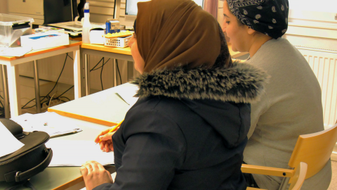 Kaksi henkilöä opiskelee pulpetin ääressä luokkahuoneessa.