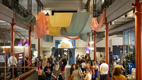 Vapriikin aulassa paljon ihmisiä, taustalla Olipa kerran -näyttelyn sisääntulo. Katossa kangaskoristeita roikkumassa.