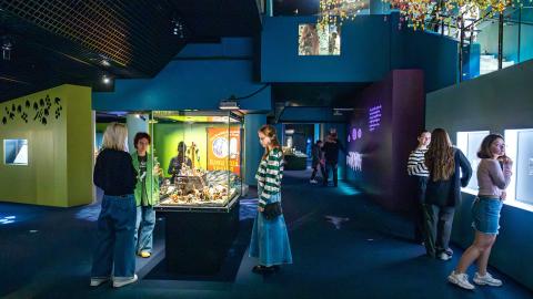 Hämärässä sinertävässä museotilassa on runsaasti ihmisitä tutkimassa valaistuja vitriineitä. 