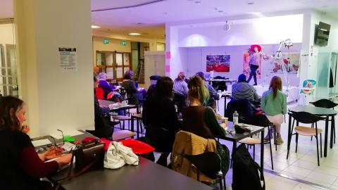 Pikapiirustustyöpaja kahvilamiljöössä. Etualalla opiskelijoita. Taustalla on elävä malli.