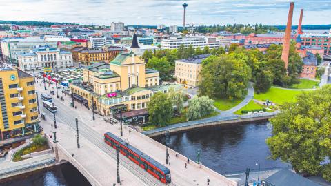Punainen ratikka ajaa Hämeensiltaa pitkin kohti Tampereen Keskustoria kesäisenä päivänä ja taustalla horisontissa näkyy Näsinneula.