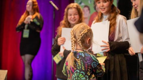 Lapsi ottaa vastaan kunniakirjaa kolmelta massiraadin jäseneltä