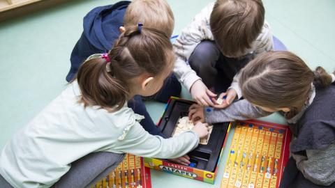 Neljä lasta istuu ringissä ja pitää käsiä keskellä päällekkäin.