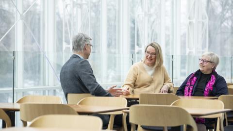 Kolme henkilöä istuu keskustelemassa pöydän ääressä.