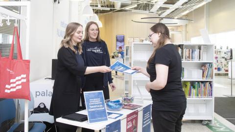 Kaksi kaupungin työntekijää keskustelemassa asukkaan kanssa. Toinen työntekijöistä ojentaa esitettä asukkaalle.