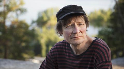 Henkilö istuu kalliolla, jonka taustalla on metsää.