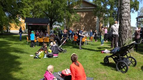 Eri ikäisiä istumassa puistossa. Kuvan etualalla aikuinen ja lapsi viltin päällä.