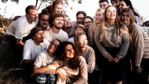 Ryhmä nuoria aikuisia hymyilee ja katselee kohti taivaanrantaa.