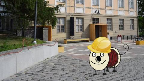 Taustalla vaalea vanha kivirakennus, jonka edessä mukulakivipiha. Edustalla piirretty Rulla-hahmo seisoo päässään keltainen rakennuskypärä.