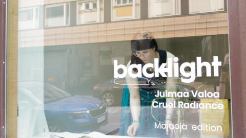 Nuori nainen on liiketilan näyteikkunassa. Hän tekee töitä.