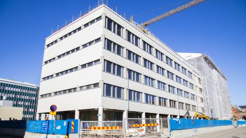 Valkoinen virastotalon etualalla ei näy enää rakentamisen aikaista suojahuppua, mutta osassa taloa se vielä on. Talon ympärillä on rakentamisen aikainen aita.