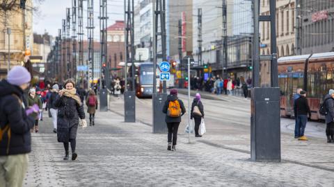 Katunäkymä. Rakennuksia, ihmisiä, raitiovaunu ja metallipylväitä.