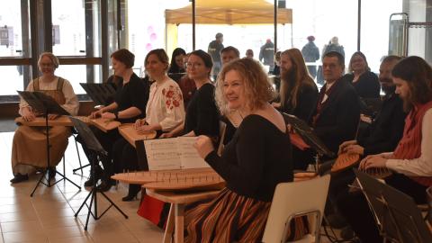 Henkilö soittaa kannelta. Hänen takanaan on ryhmä muita soittajia.