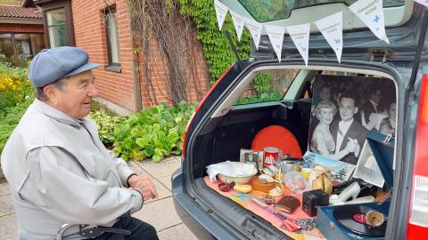 Harmaatakkinen mies katselee auton tavaratilaan aseteltua Peräkonttimuseon näyttelyä.