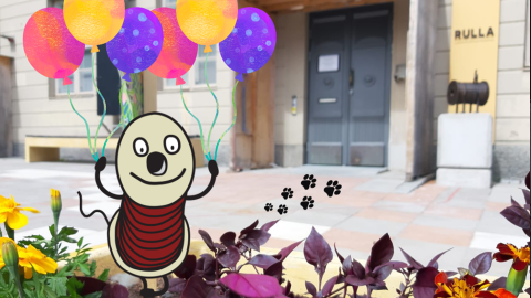 Piirretty Rulla-hahmo pitää tassuissaan keltaisia, violetteja ja vaaleanpunaisia ilmapalloja. Taustalla Rullan sisäänkäynti.