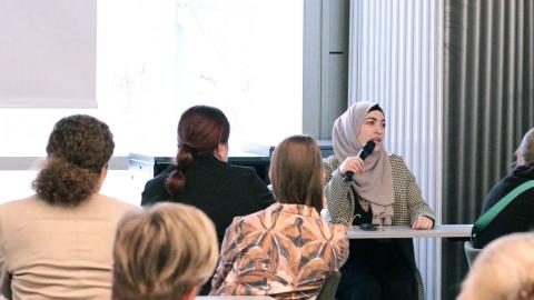 Henkilö puhuu monimuotoiselle yleisölle kokoustilassa. 