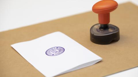 Valkoinen äänestyslippu ruskealla alustalla ja vieressä leimasin.