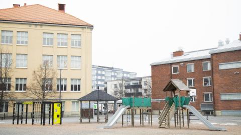 Vasemmalla vanhaa koulua, oikealla uudempaa, etualalla leikki- ja liikuntavälineitä.