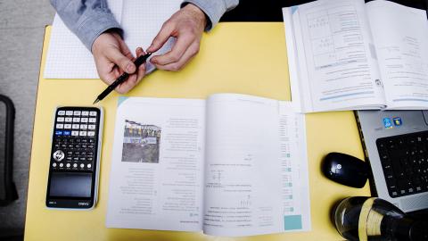 A student sitting at a desk studying with books and a calculator.