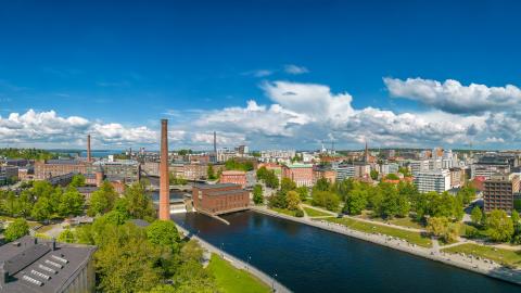 Kaupunkimaisema. Etualalla vettä, keskellä punatiilinen tehtaanpiippu.