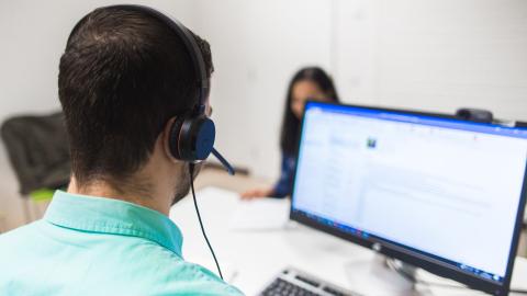 Henkilö katsoo tietokonetta kuulokkeet päässä.