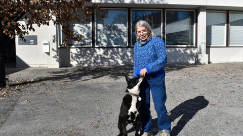 A person stands in front of the school with their dog. The dog sniffs the owner&#039;s hands.