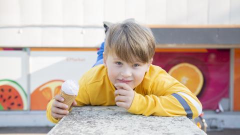 Keltapuseroinen poika nojaa pöytään ja syö jäätelöä.